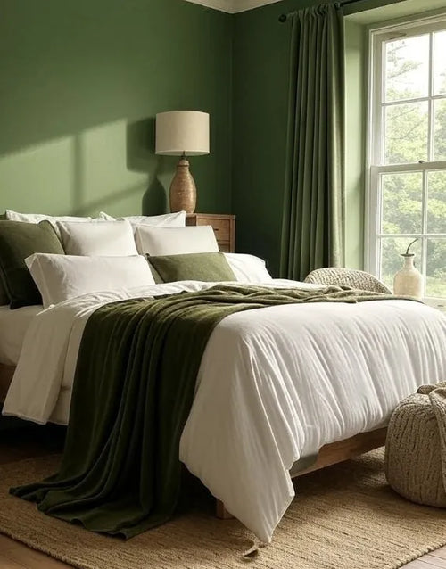Cozy bedroom with green walls, a bed with white bedding and green throw, and a lamp.