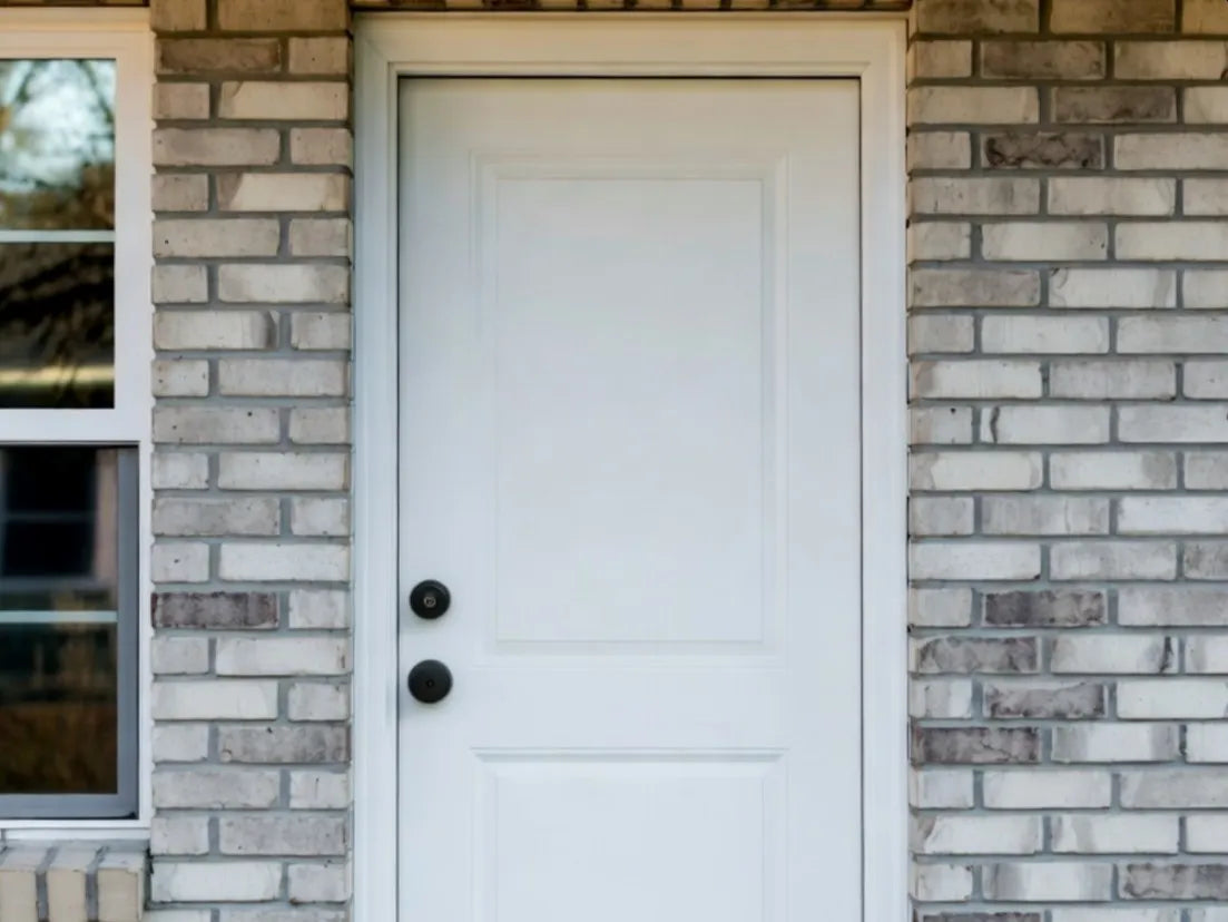 White door with black doorknobs on a brick wall
